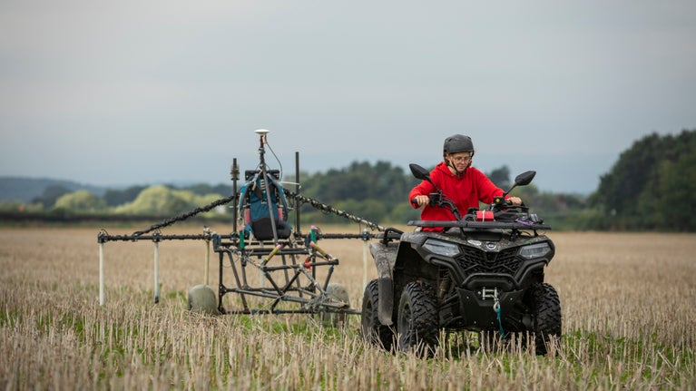 Archaeologist carrying out geophysical survey on a quadbike through a field